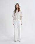 Woman wearing a beige top and white pants on a white background