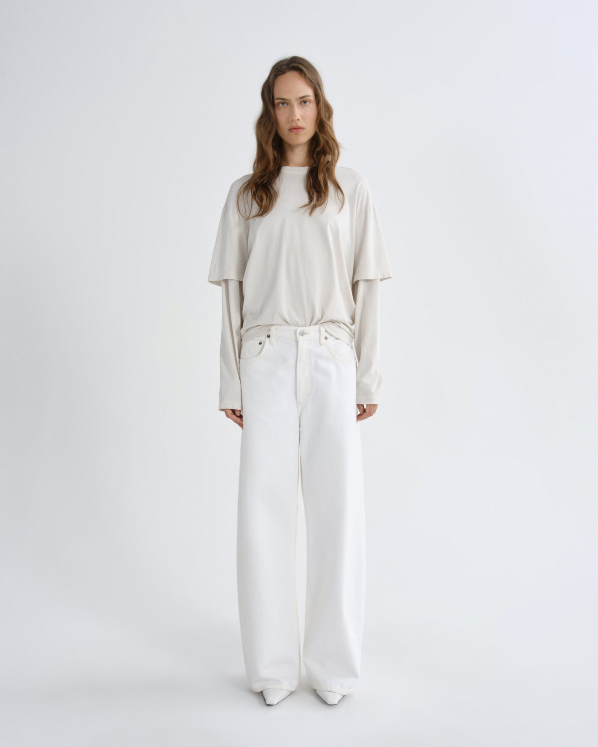Woman wearing a beige top and white pants on a white background