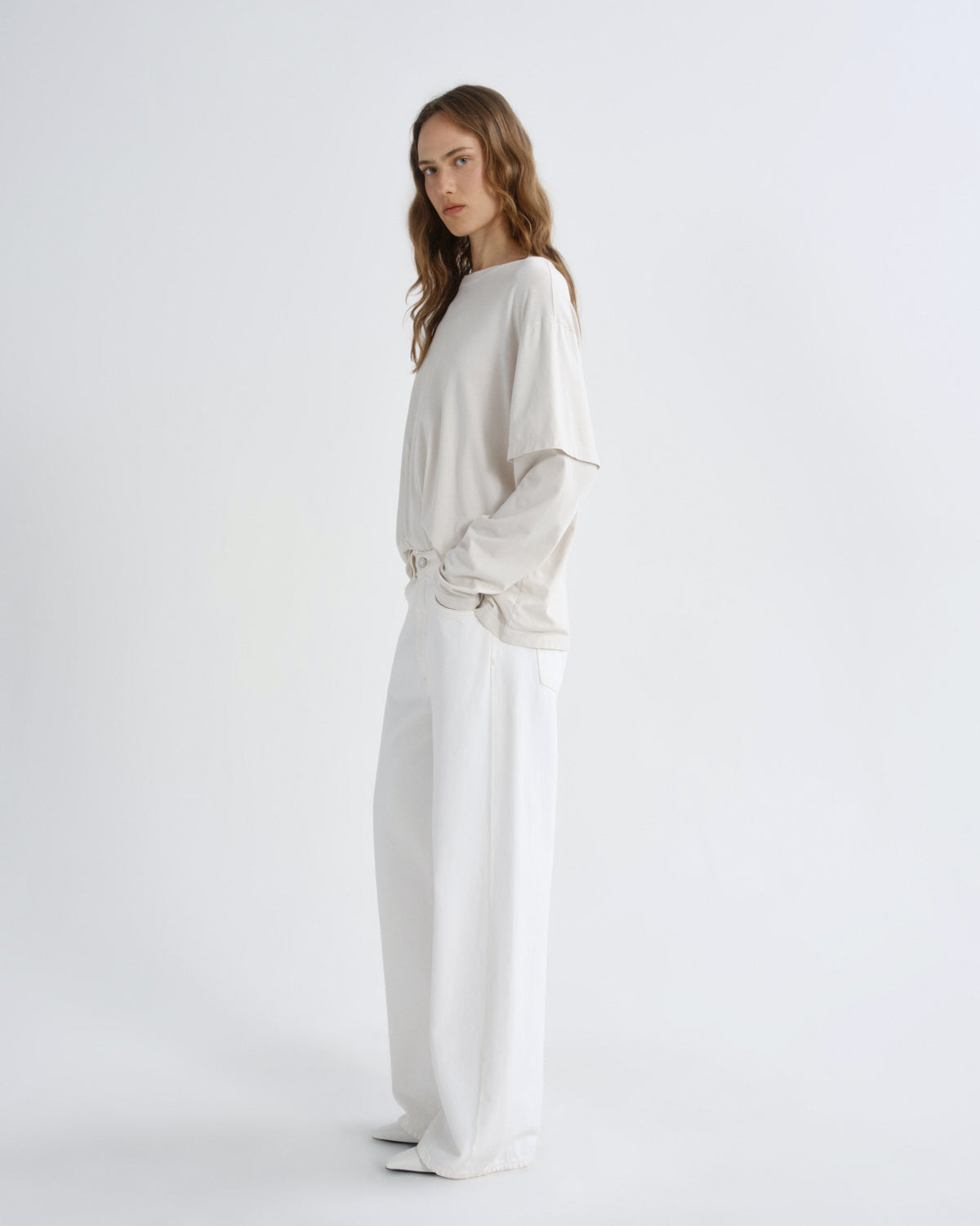 Woman wearing a beige sweater and white pants on a white background