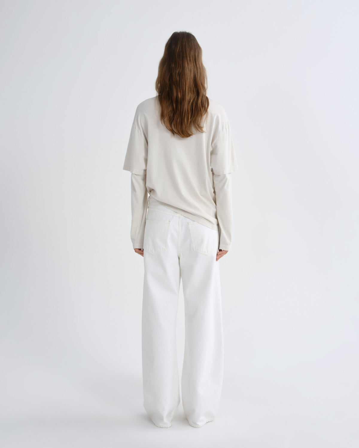 Person wearing a beige top and white pants on a white background