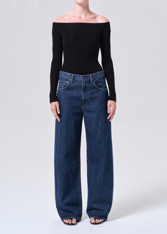 Person wearing a black off-shoulder top and blue jeans on a white background