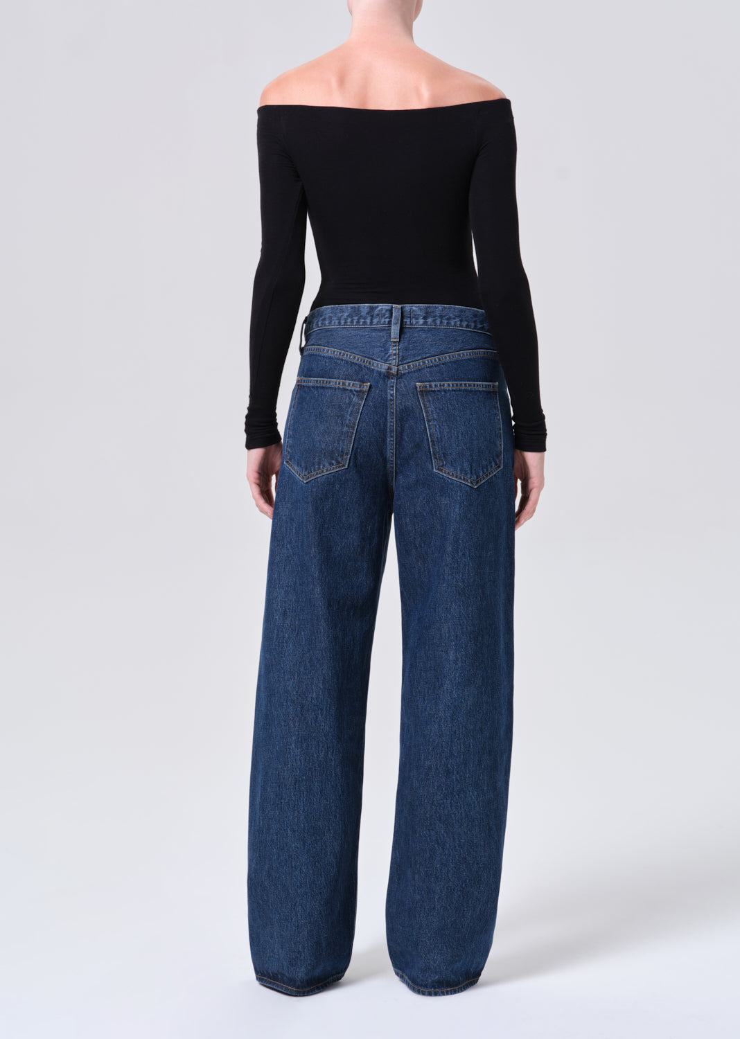 Person wearing blue jeans and a black off-shoulder top on a white background