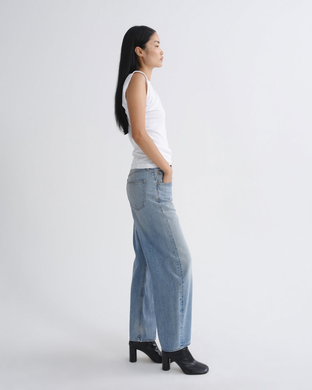 Woman wearing a white tank top and light blue jeans on a white background