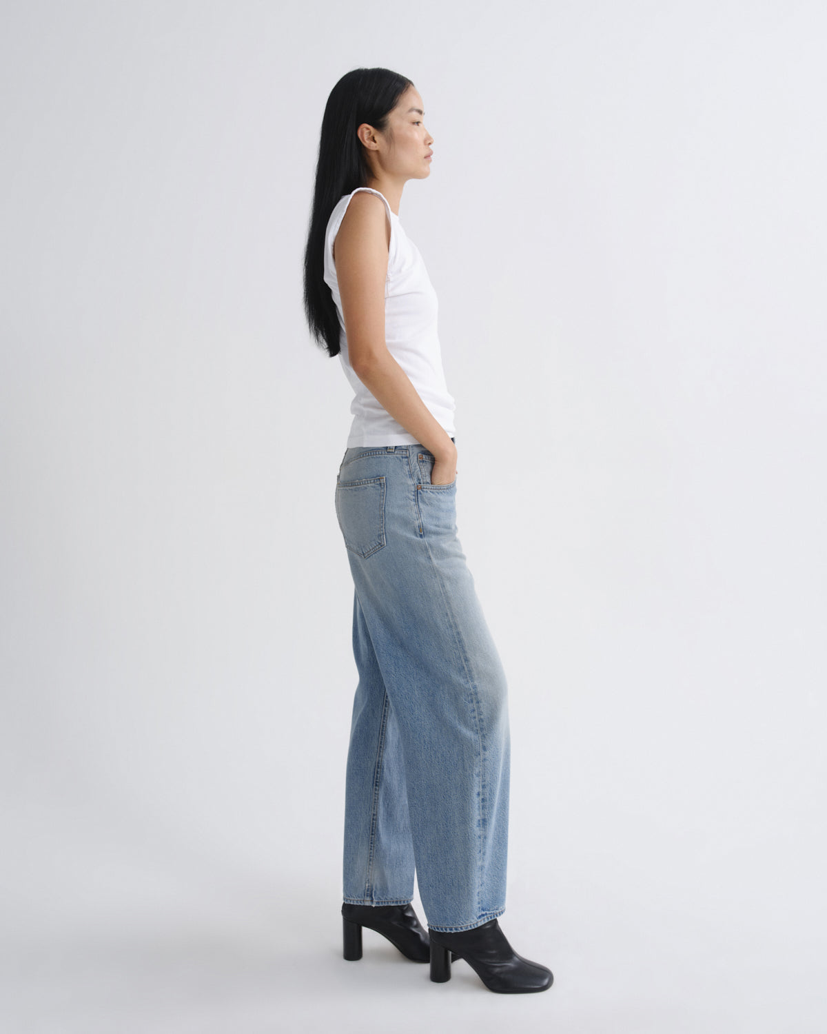 Woman wearing a white tank top and light blue jeans on a white background