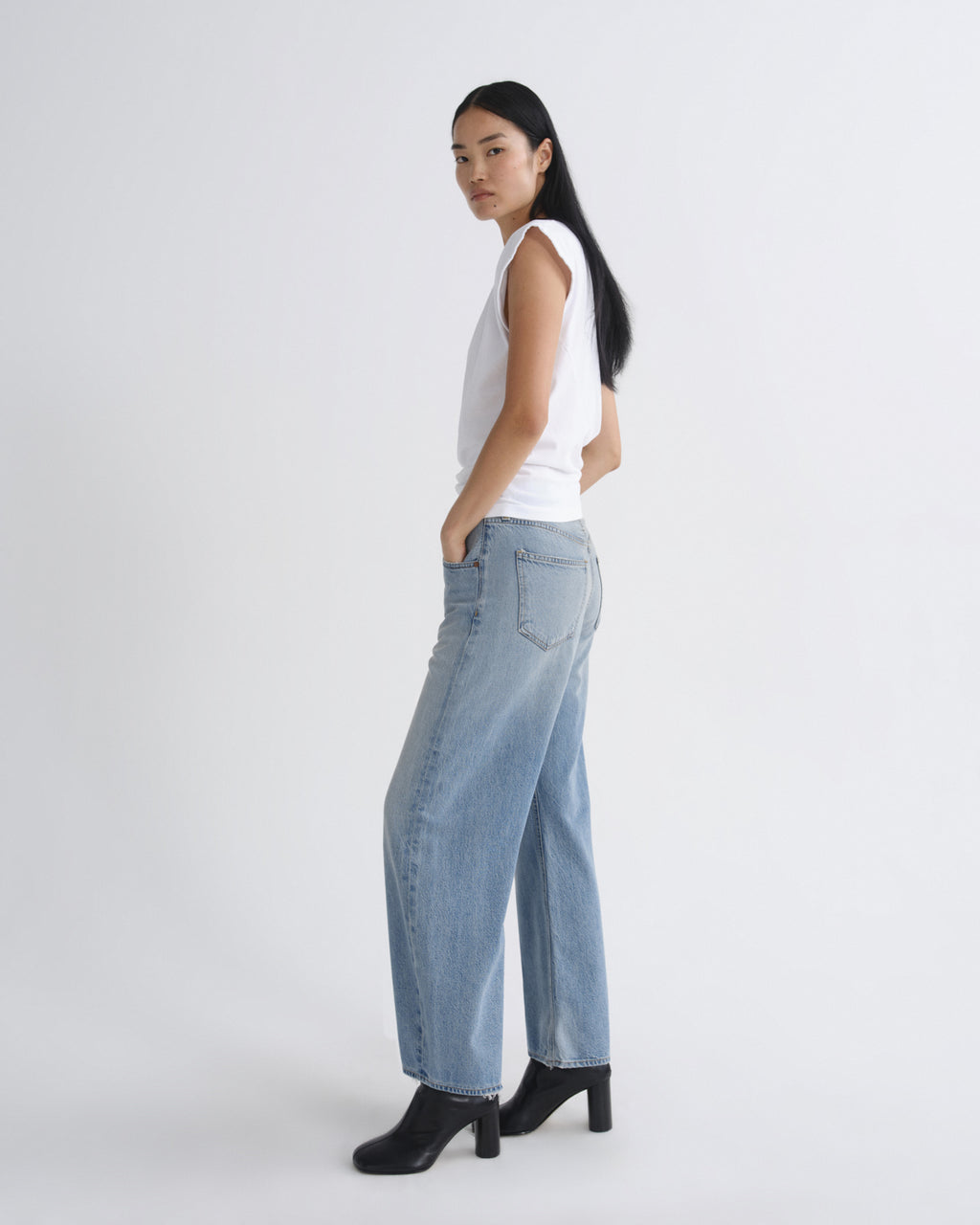 Woman wearing light blue jeans and a white top on a white background