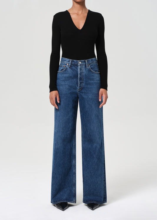 Person wearing a black long-sleeve top and blue jeans on a white background