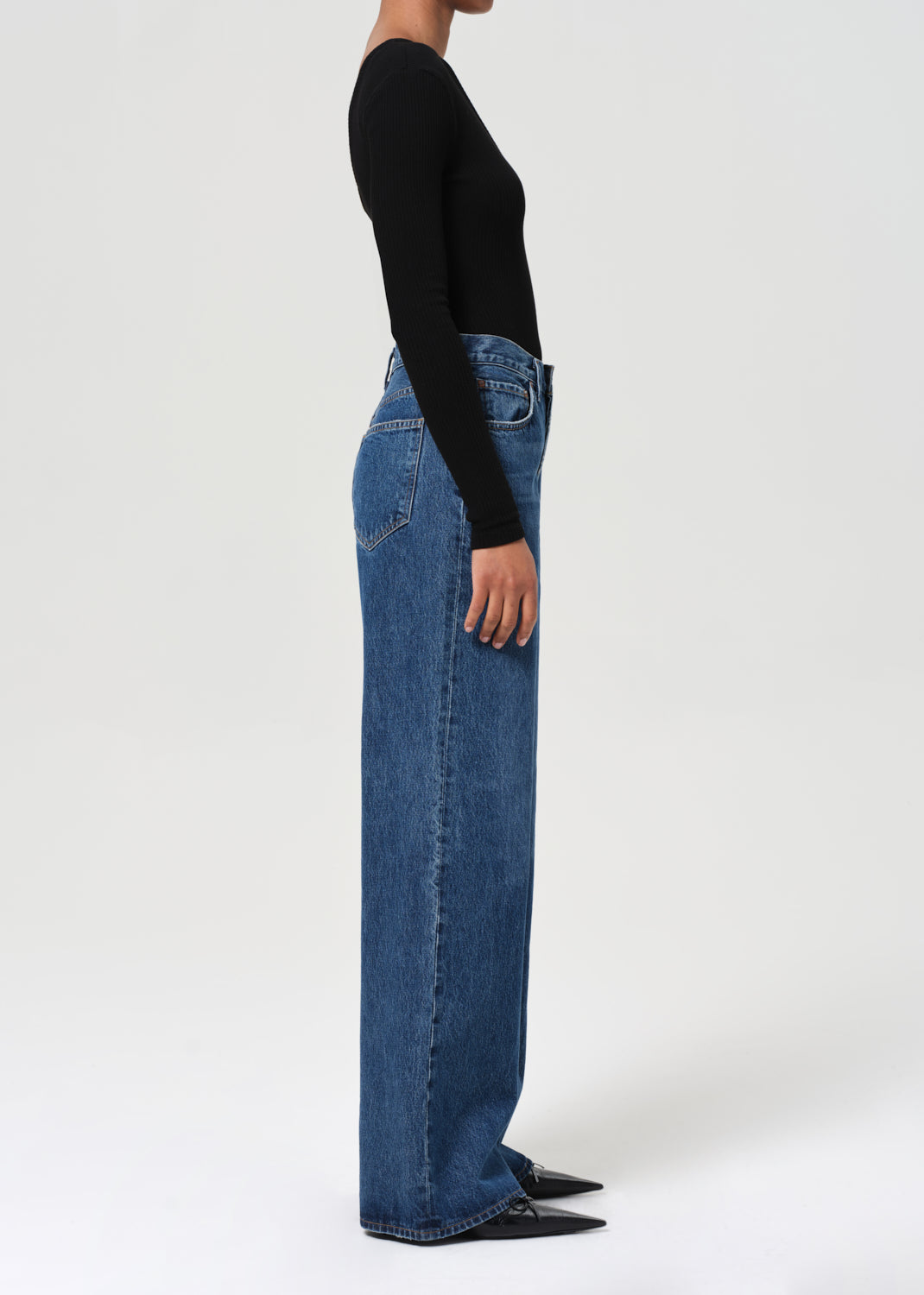 Person wearing blue jeans and a black top on a white background