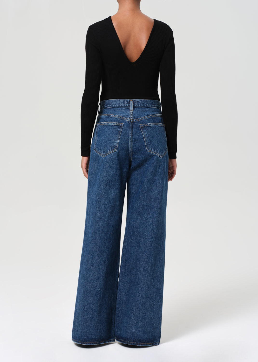 Person wearing blue jeans and a black long-sleeve top on a white background