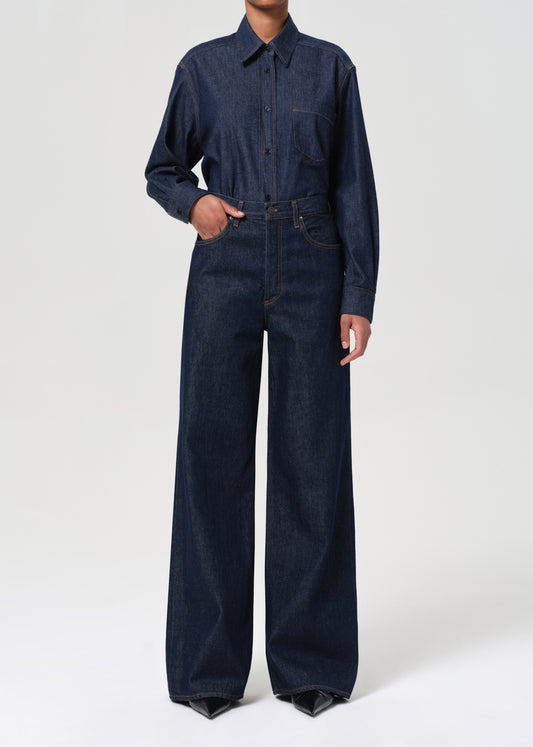 Person wearing a dark blue denim jumpsuit on a white background