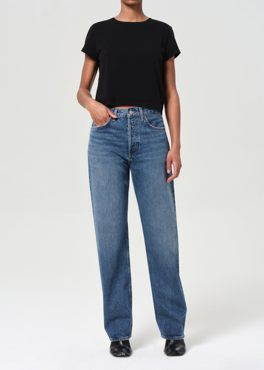 Person wearing blue jeans and a black top on a white background