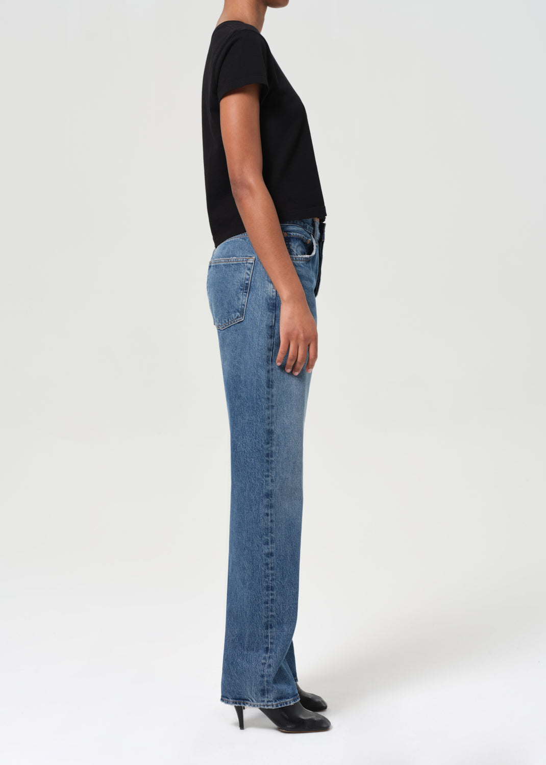 Person wearing blue jeans and a black top on a white background