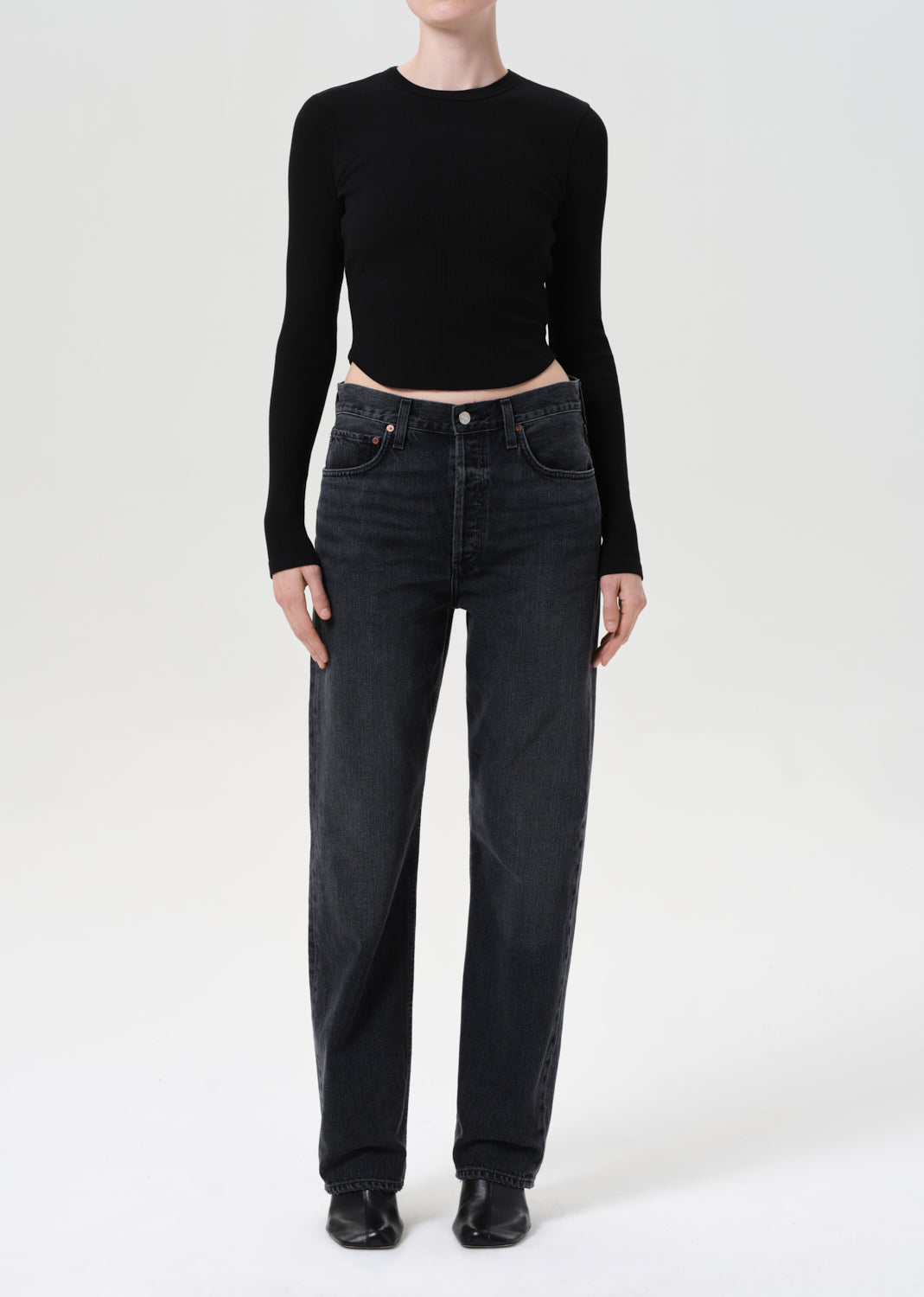 Person wearing a black long-sleeve top and dark jeans on a white background
