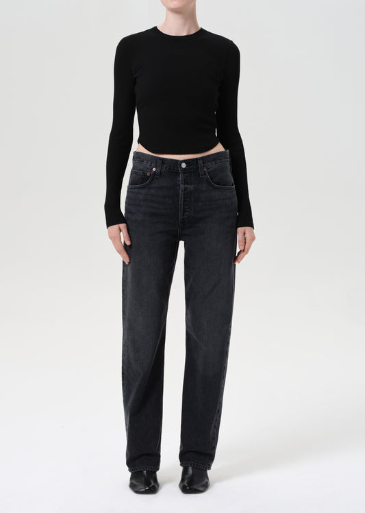 Person wearing a black long-sleeve top and dark jeans on a white background