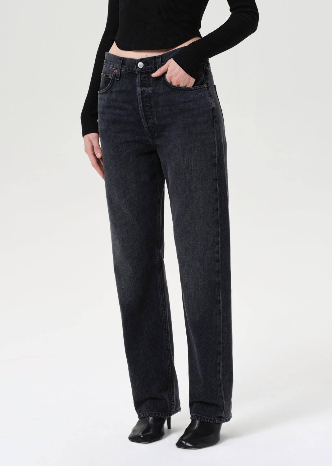 Person wearing black high-waisted jeans and a black top on a white background