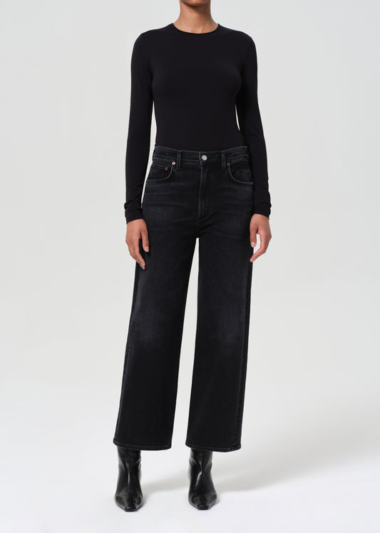 Person wearing a black long-sleeve top and black wide-leg jeans on a white background