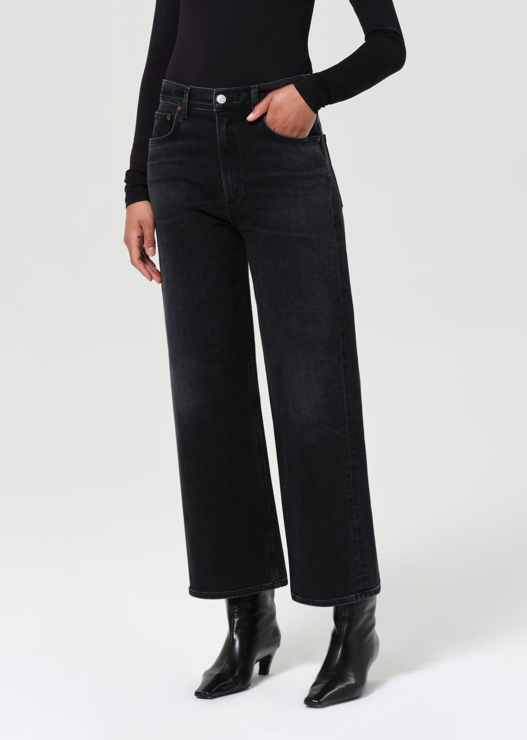 Person wearing black high-waisted jeans and black boots on a white background