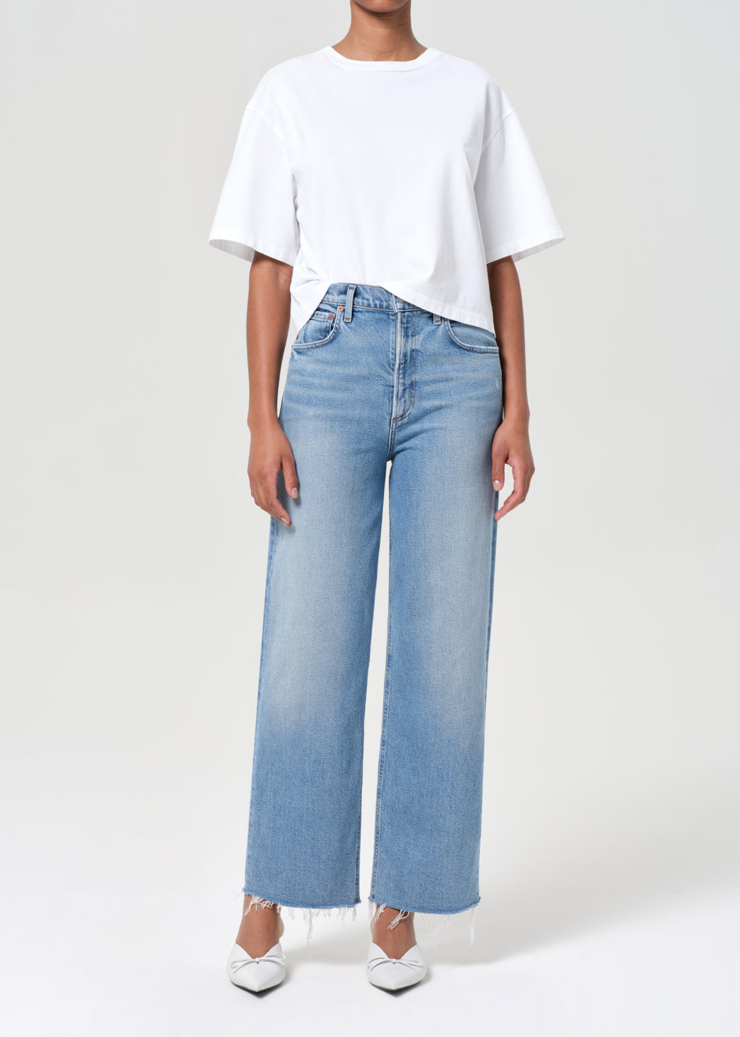 Person wearing a white t-shirt and light blue jeans on a plain background