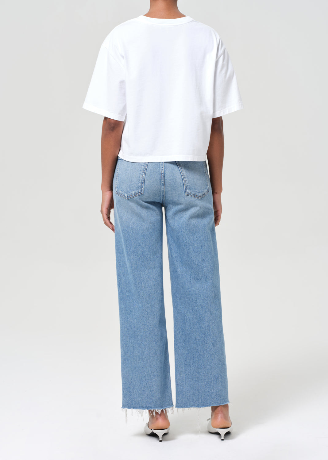 Person wearing a white t-shirt and light blue jeans on a plain background