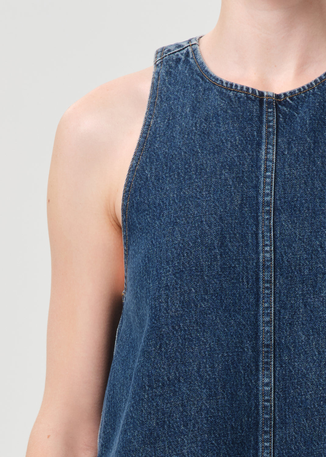 Close-up of a person wearing a blue denim sleeveless top on a light gray background