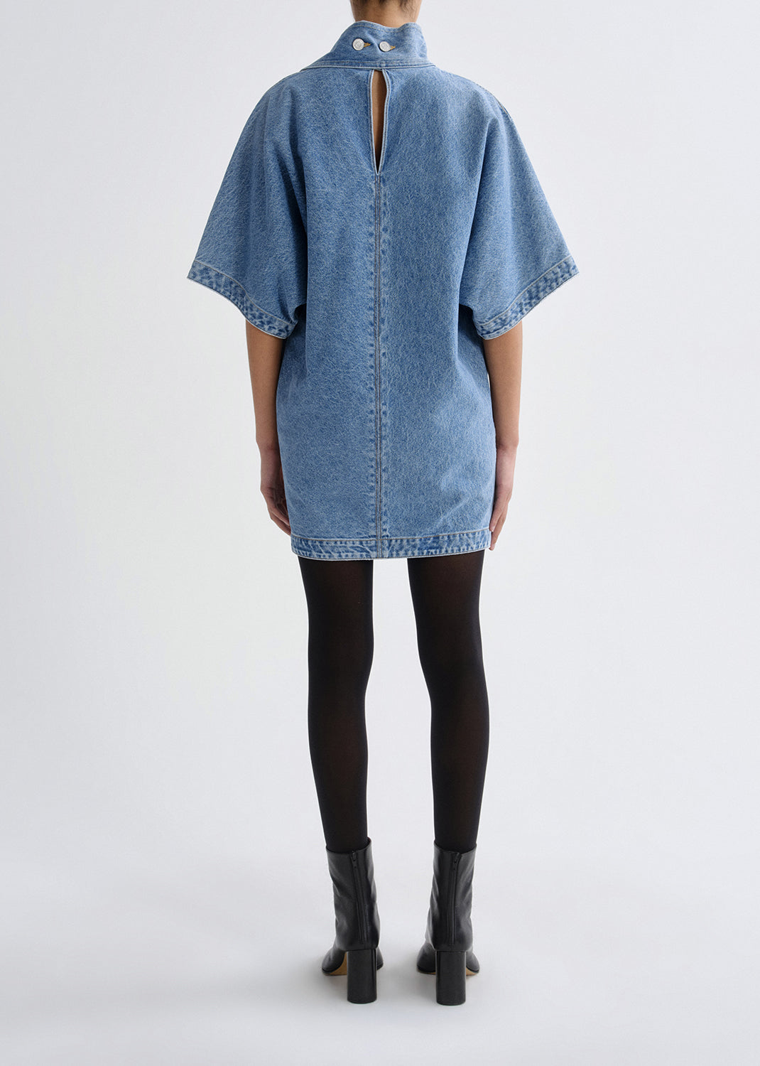 Person wearing a denim dress with a cutout back on a grey background