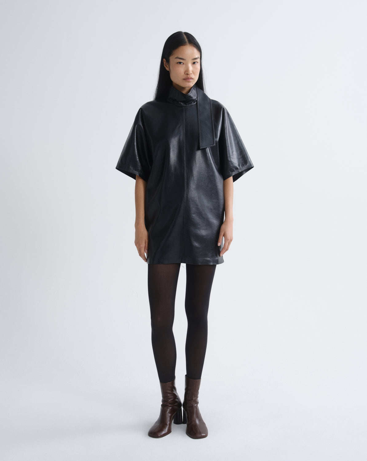 Person wearing a black leather mini dress on a grey background