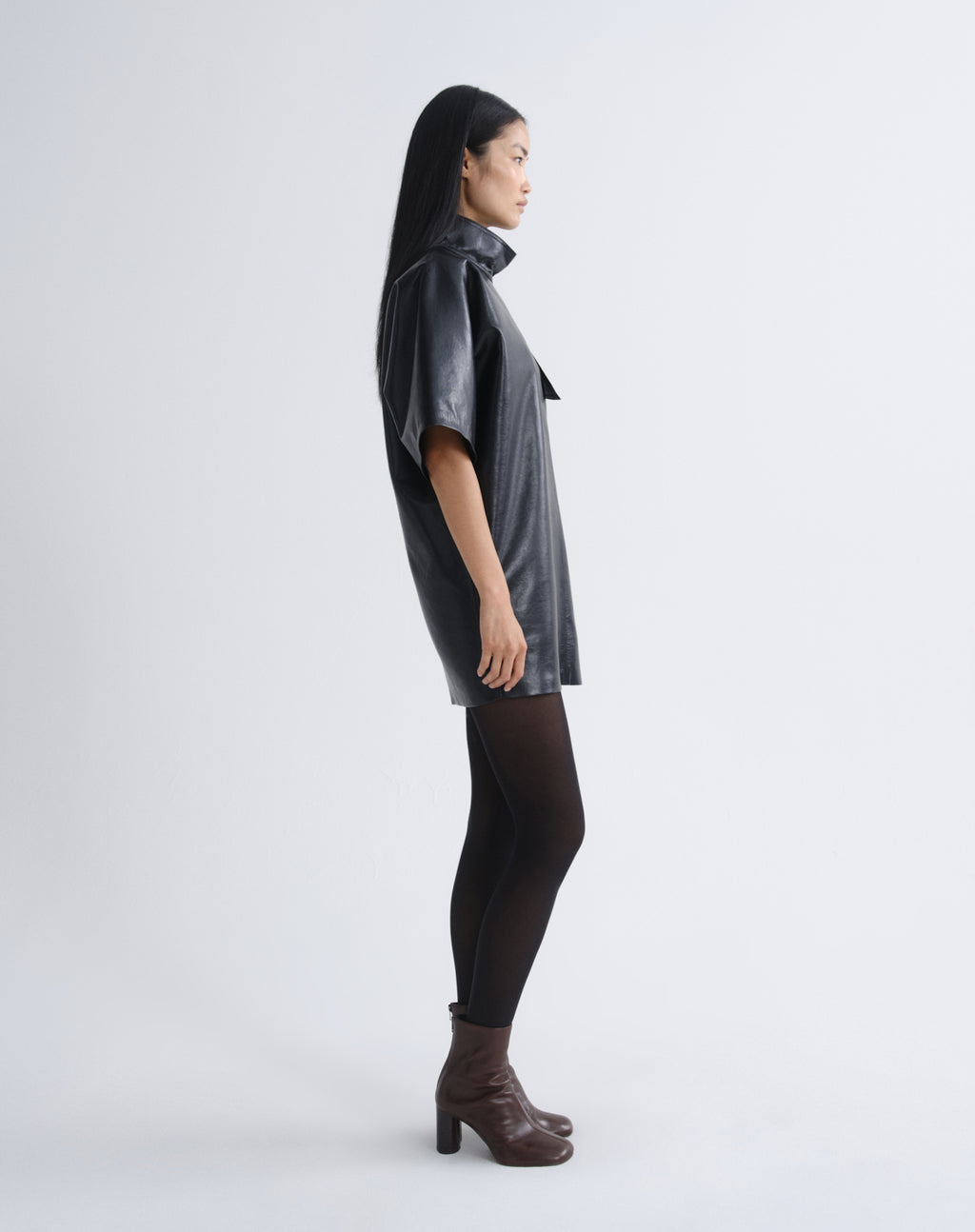 Person wearing a black leather mini dress viewed from the side on a grey background