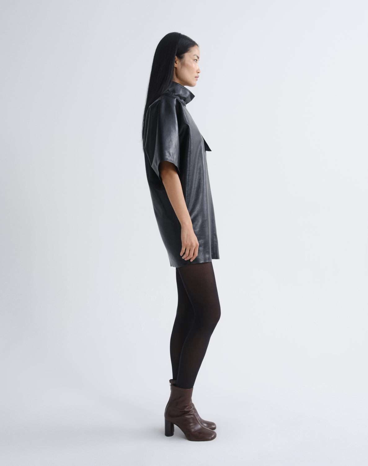 Person wearing a black leather mini dress viewed from the side on a grey background