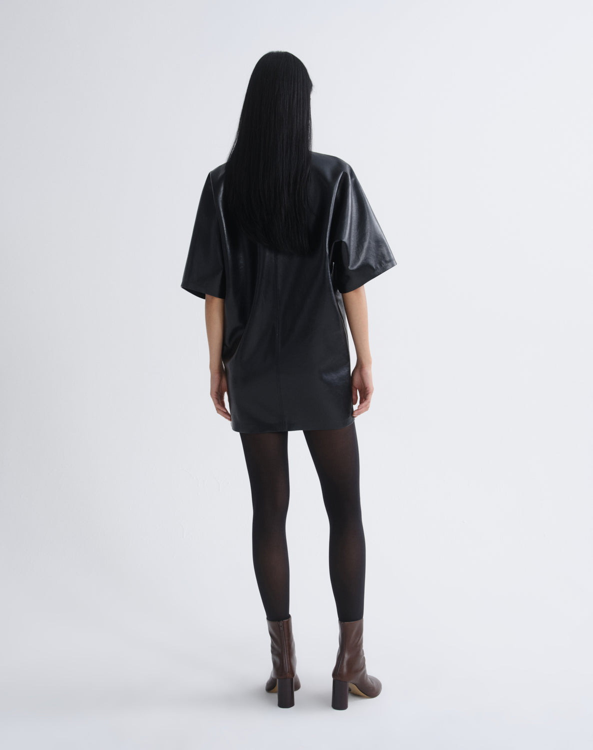 Person wearing a black leather mini dress viewed from the back on a grey background