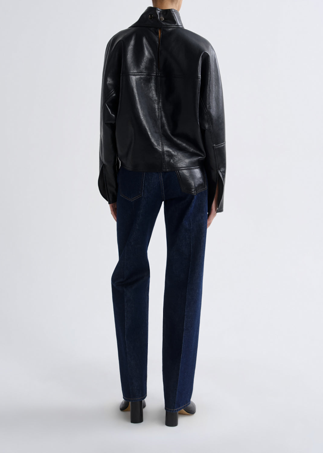 A model shown from the back wearing a black leather jacket and dark blue jeans against a grey background.