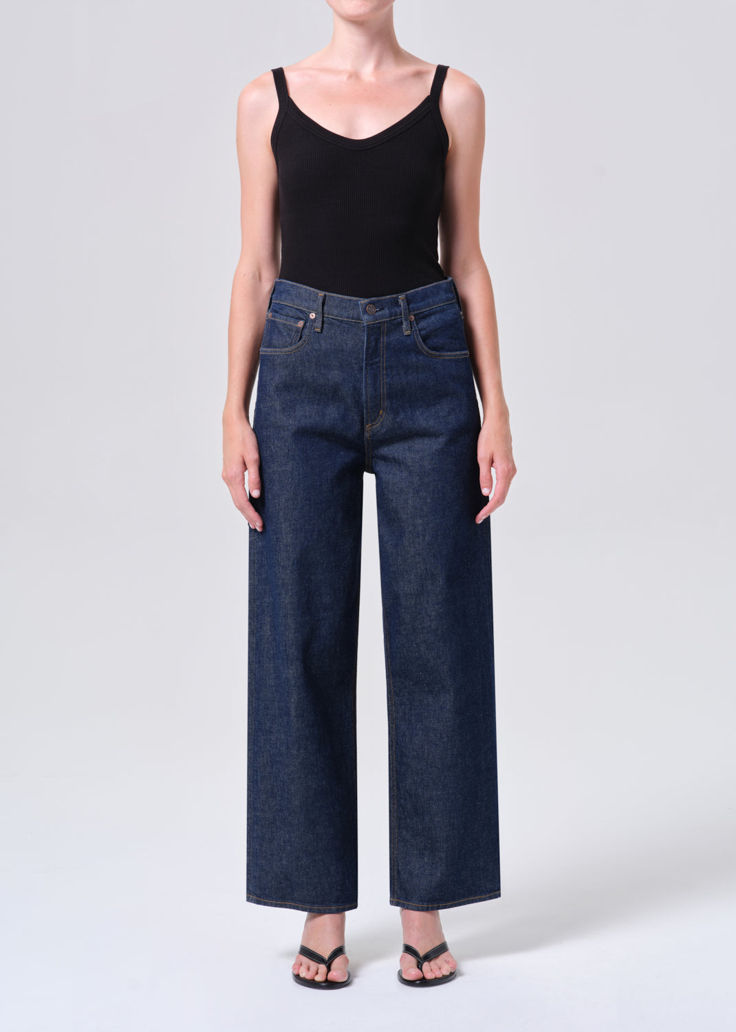 Person wearing dark blue jeans and a black tank top on a white background