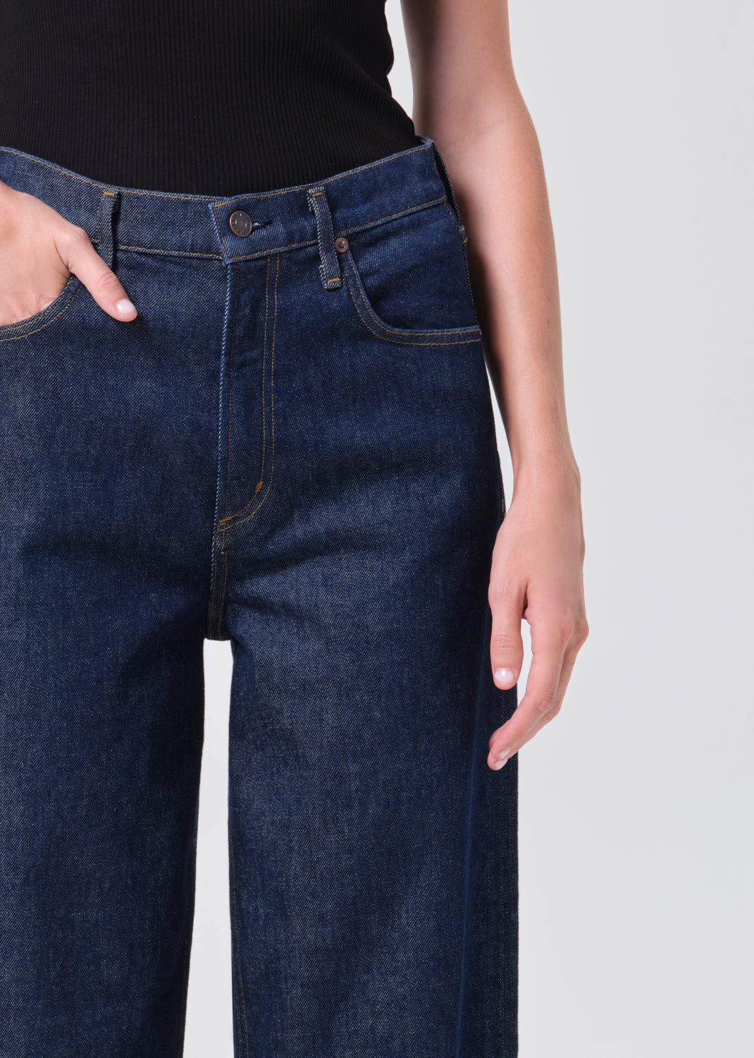 Person wearing dark blue jeans on a plain background