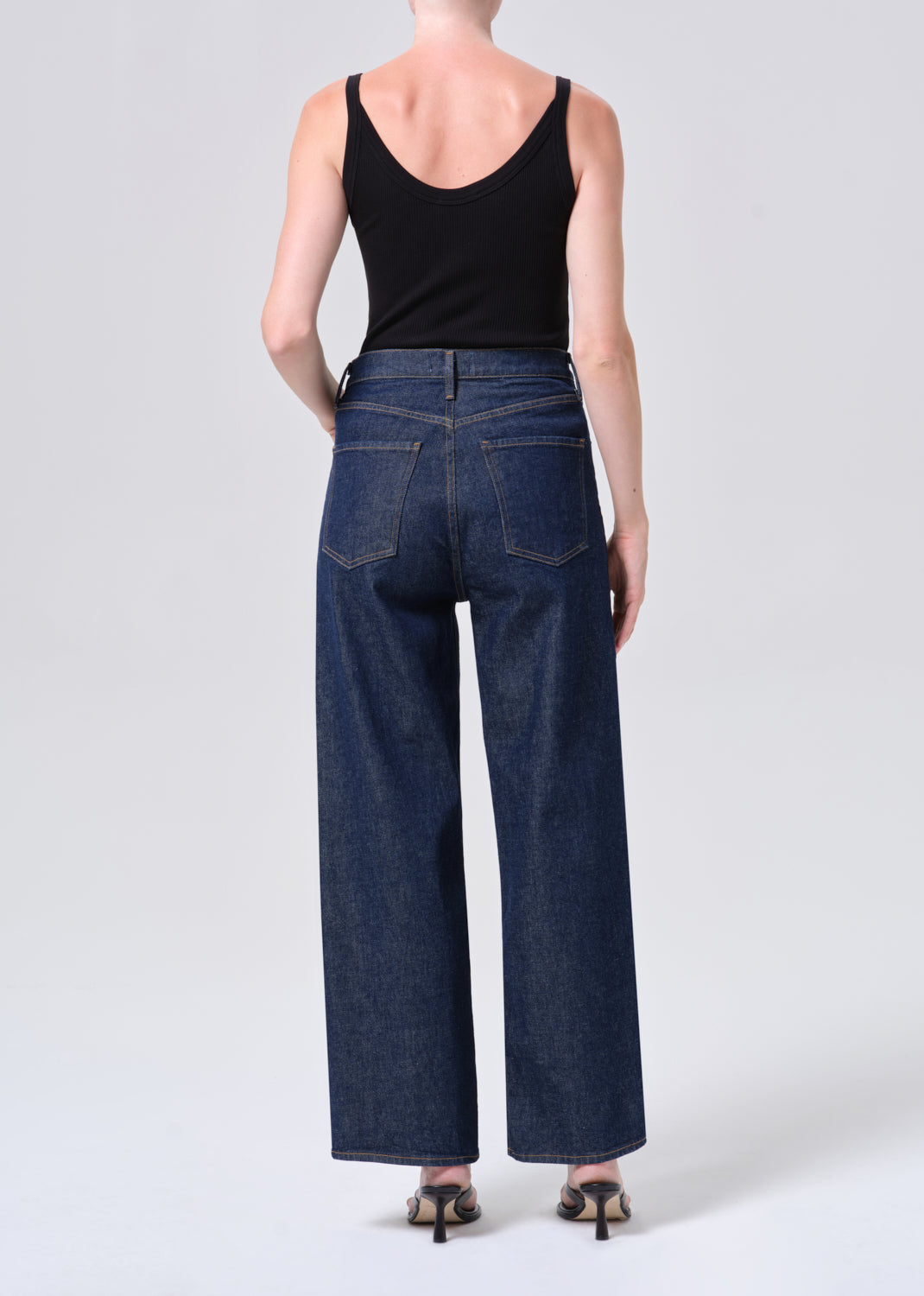 Person wearing blue jeans and a black tank top on a white background