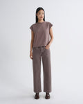 A model stands against a light gray studio background wearing a muted mauve-brown short-sleeve top and matching wide-leg pants, with dark brown boots.