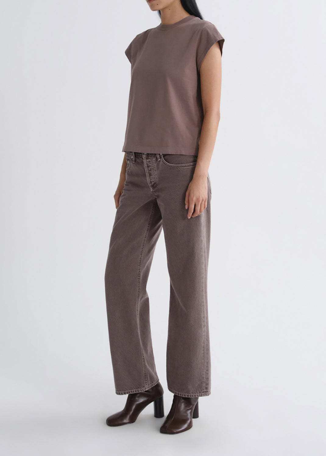 A model wearing a muted brownish-gray short-sleeve crop top, matching wide-leg jeans, and dark brown heeled ankle boots, standing against a grey background.