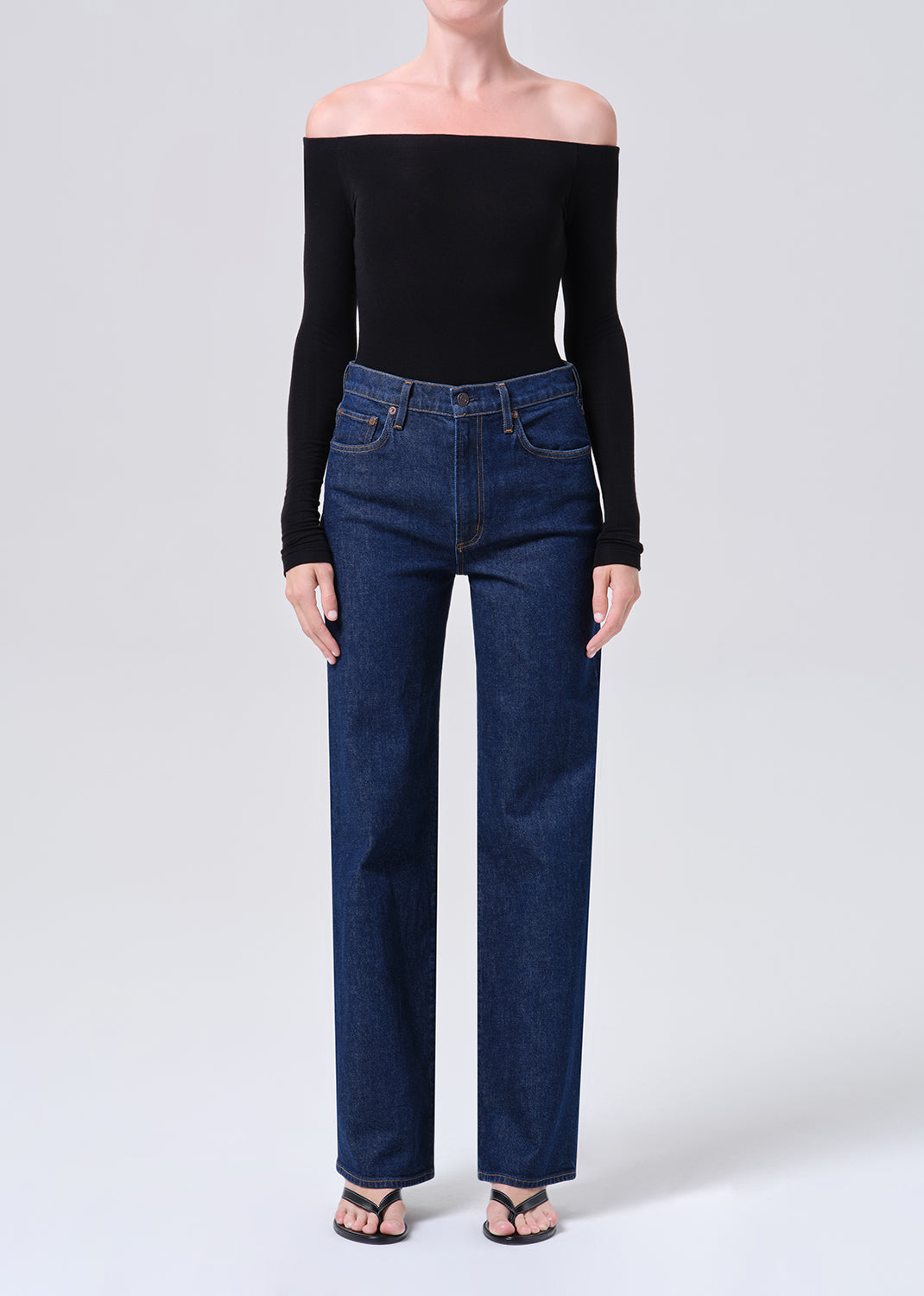 Person wearing a black off-shoulder top and blue jeans on a white background