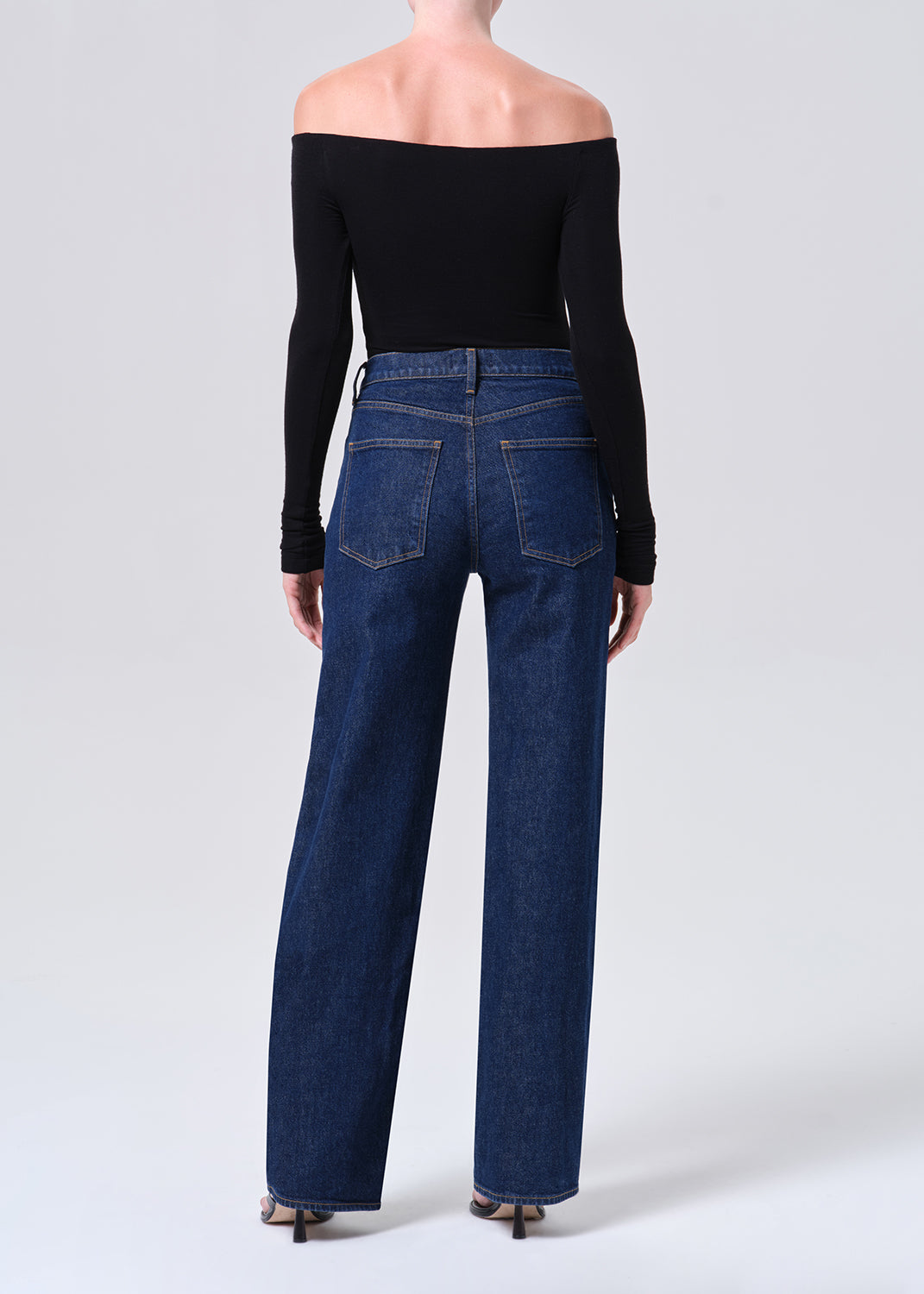 Person wearing blue jeans and a black off-shoulder top on a white background