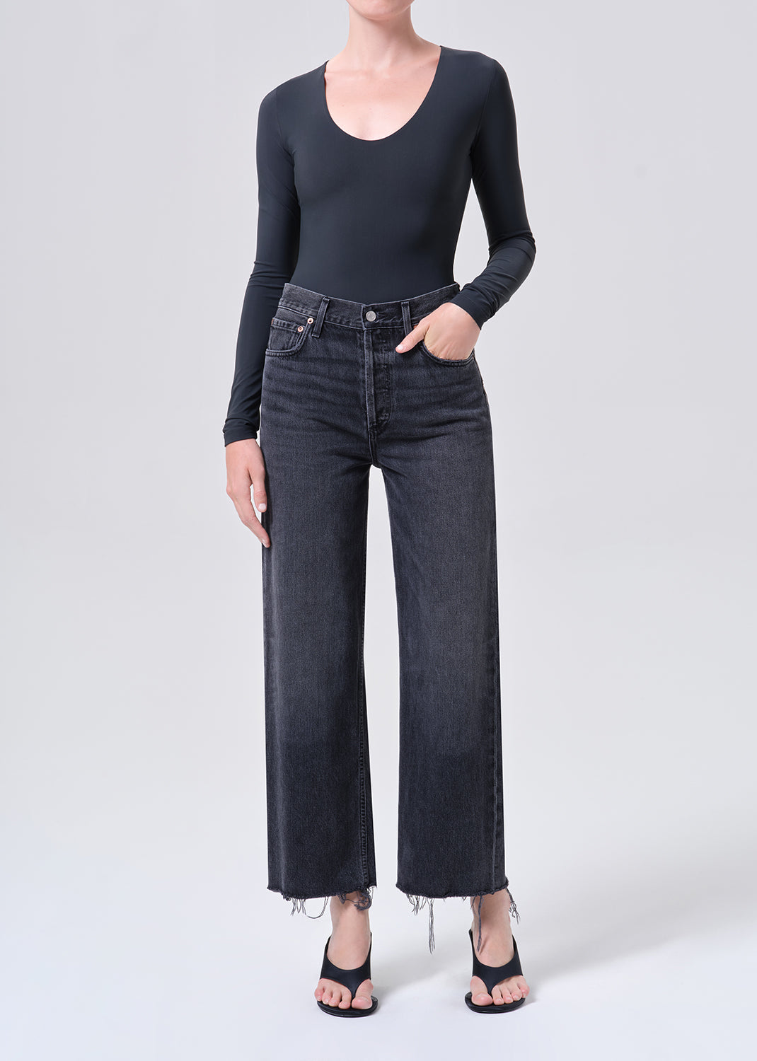 Person wearing black long-sleeve top and dark jeans on a white background