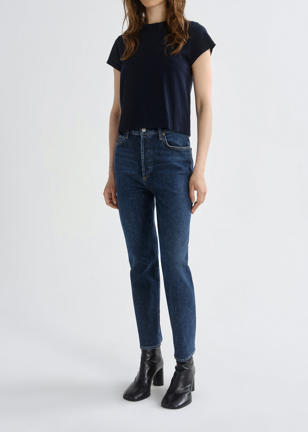 A model wearing a dark navy short-sleeve t-shirt, dark blue skinny jeans, and black leather ankle boots, standing against a grey background.