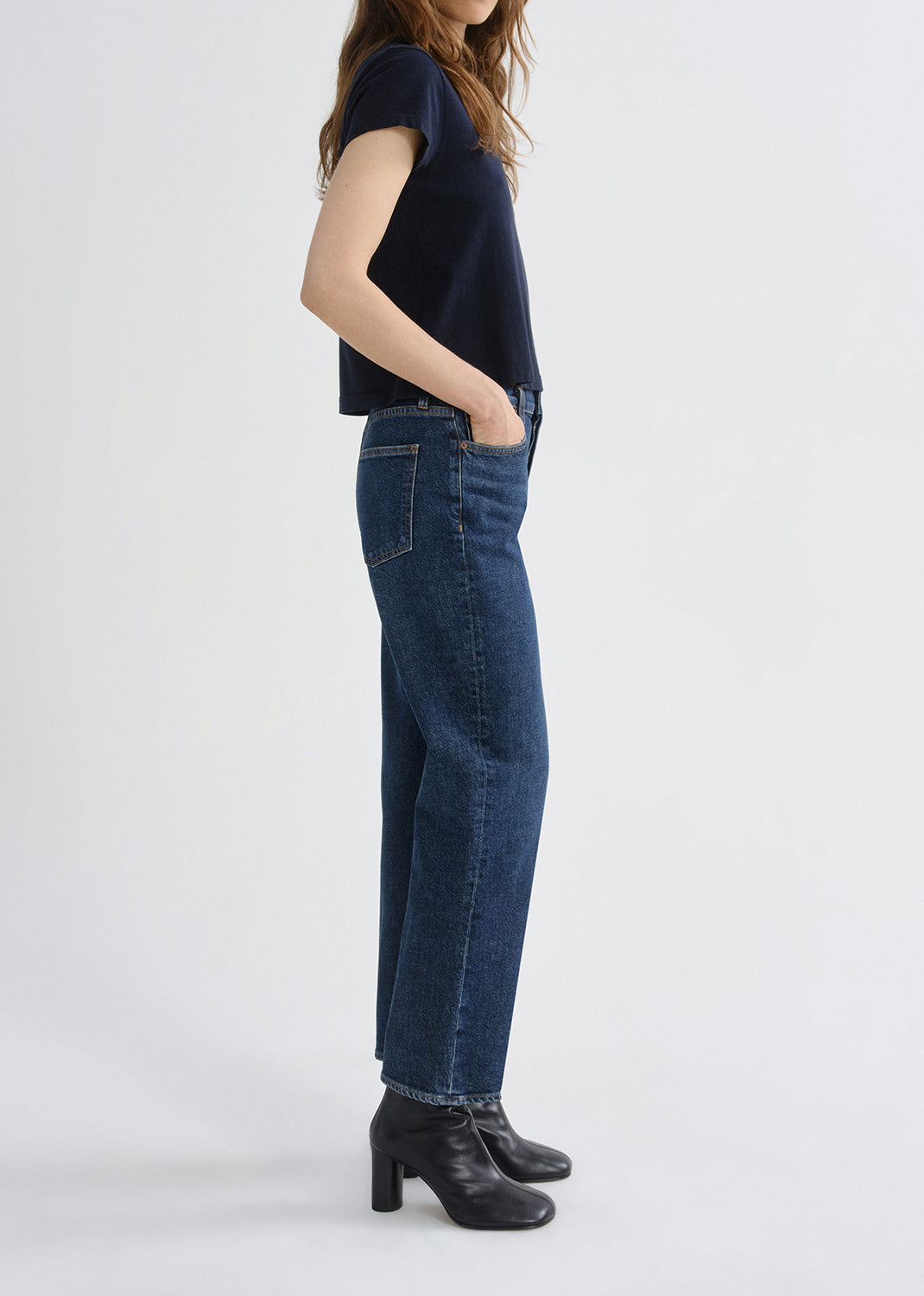 A model shown from the side wearing dark blue straight-leg jeans, a dark navy short-sleeve top, and black leather ankle boots against a grey background.