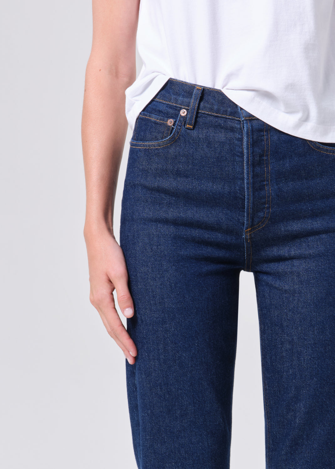 Person wearing dark blue jeans and a white shirt on a light gray background