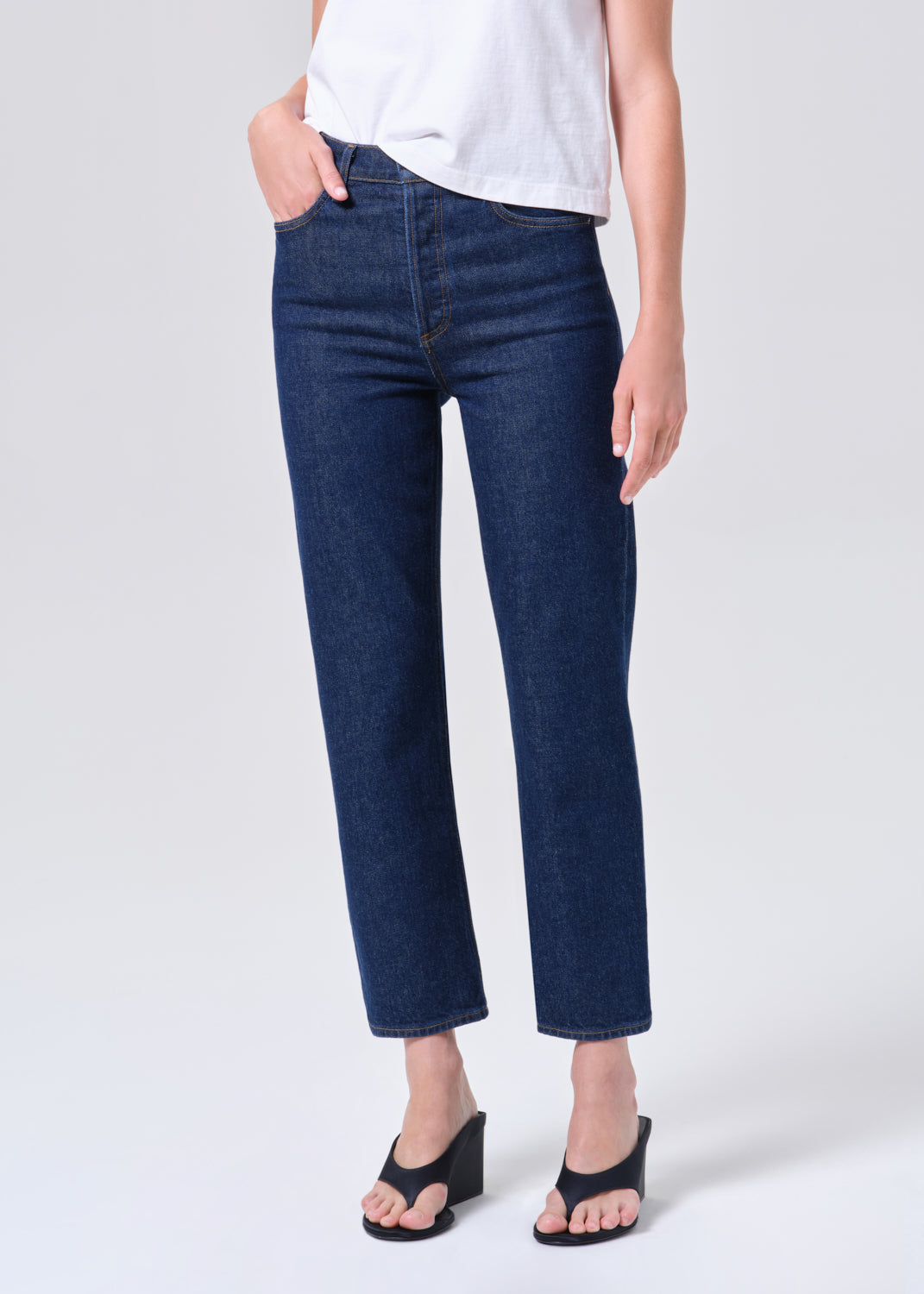 Person wearing dark blue jeans and black sandals on a white background