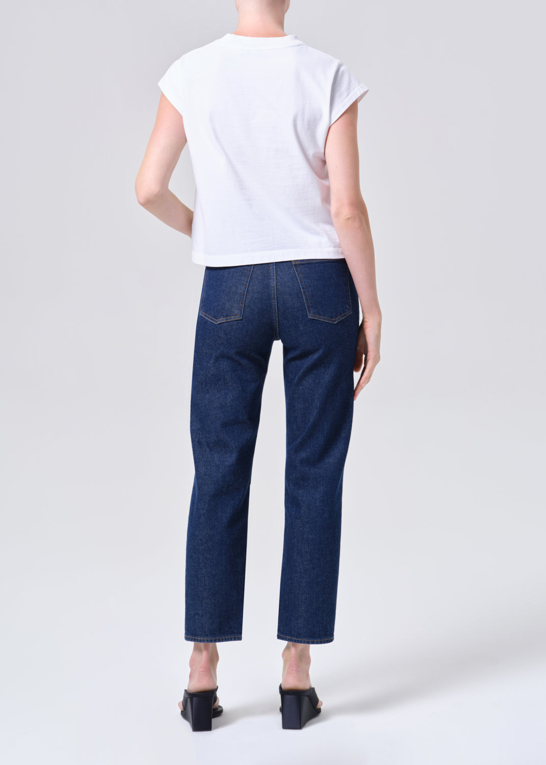 Person wearing a white t-shirt and dark blue jeans on a light gray background