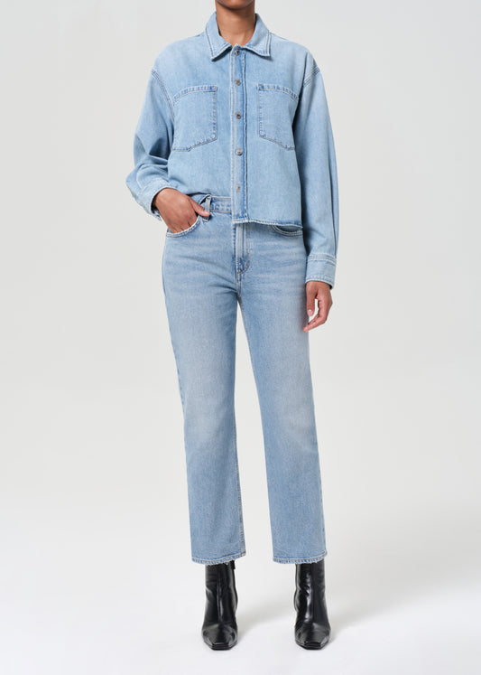 Person wearing a light blue denim jacket and jeans with black boots on a white background