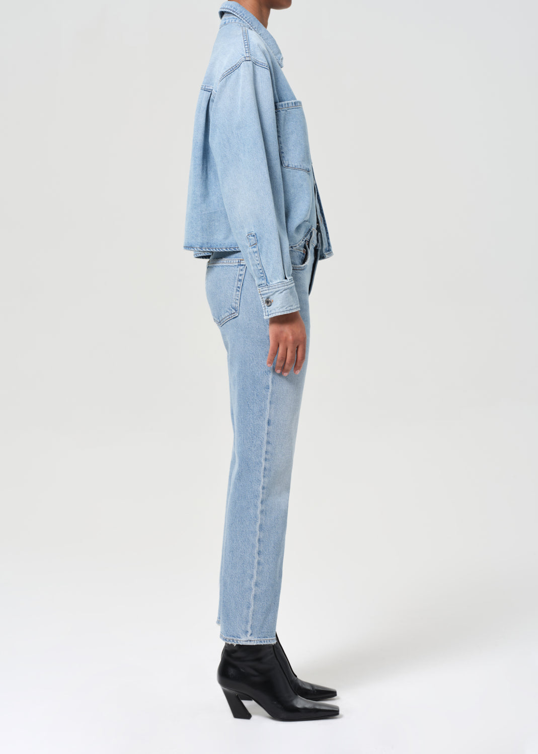 Person wearing a light blue denim jacket and jeans on a white background