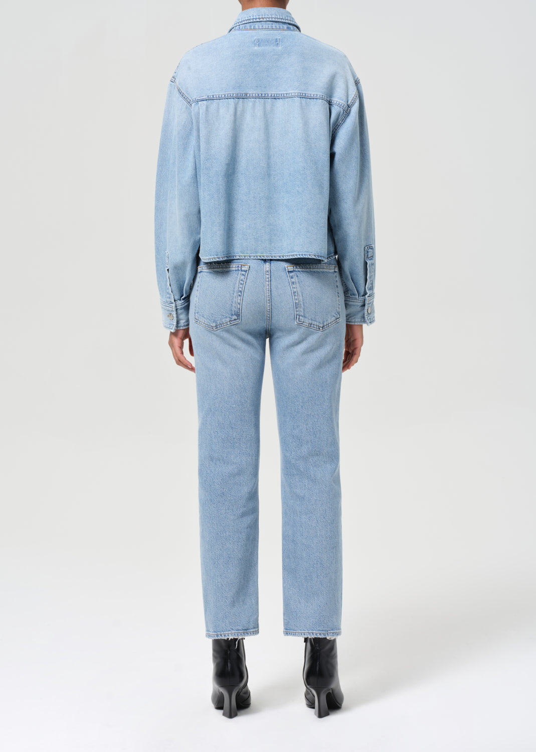 Person wearing a light blue denim jacket and jeans on a white background