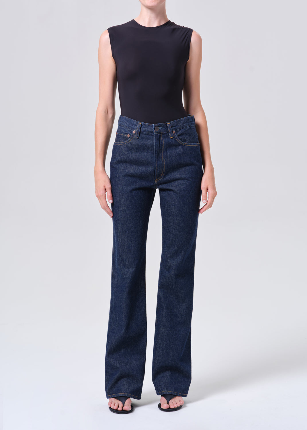 Person wearing dark blue jeans and a black sleeveless top on a white background