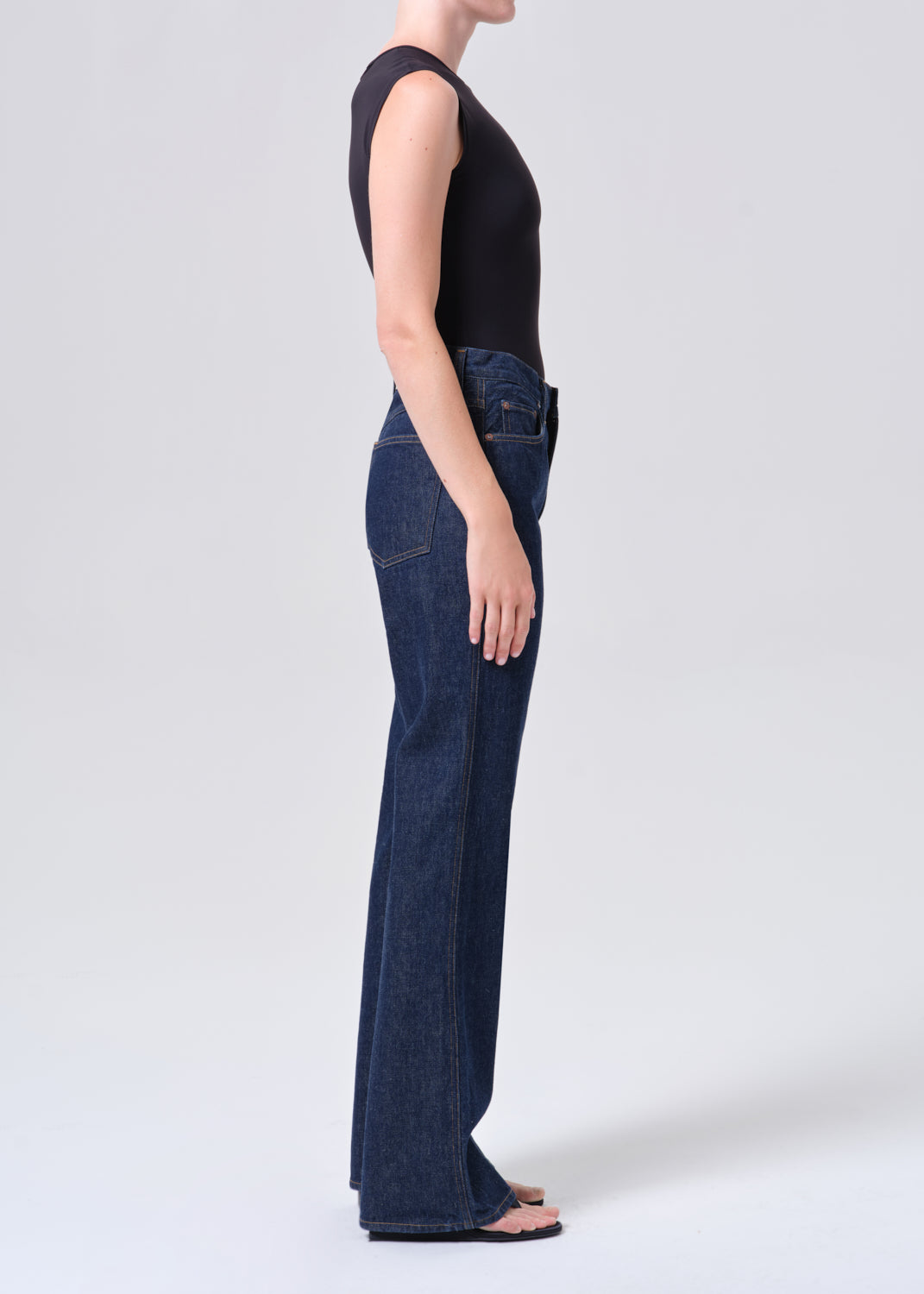 Person wearing dark blue jeans and a black sleeveless top on a white background