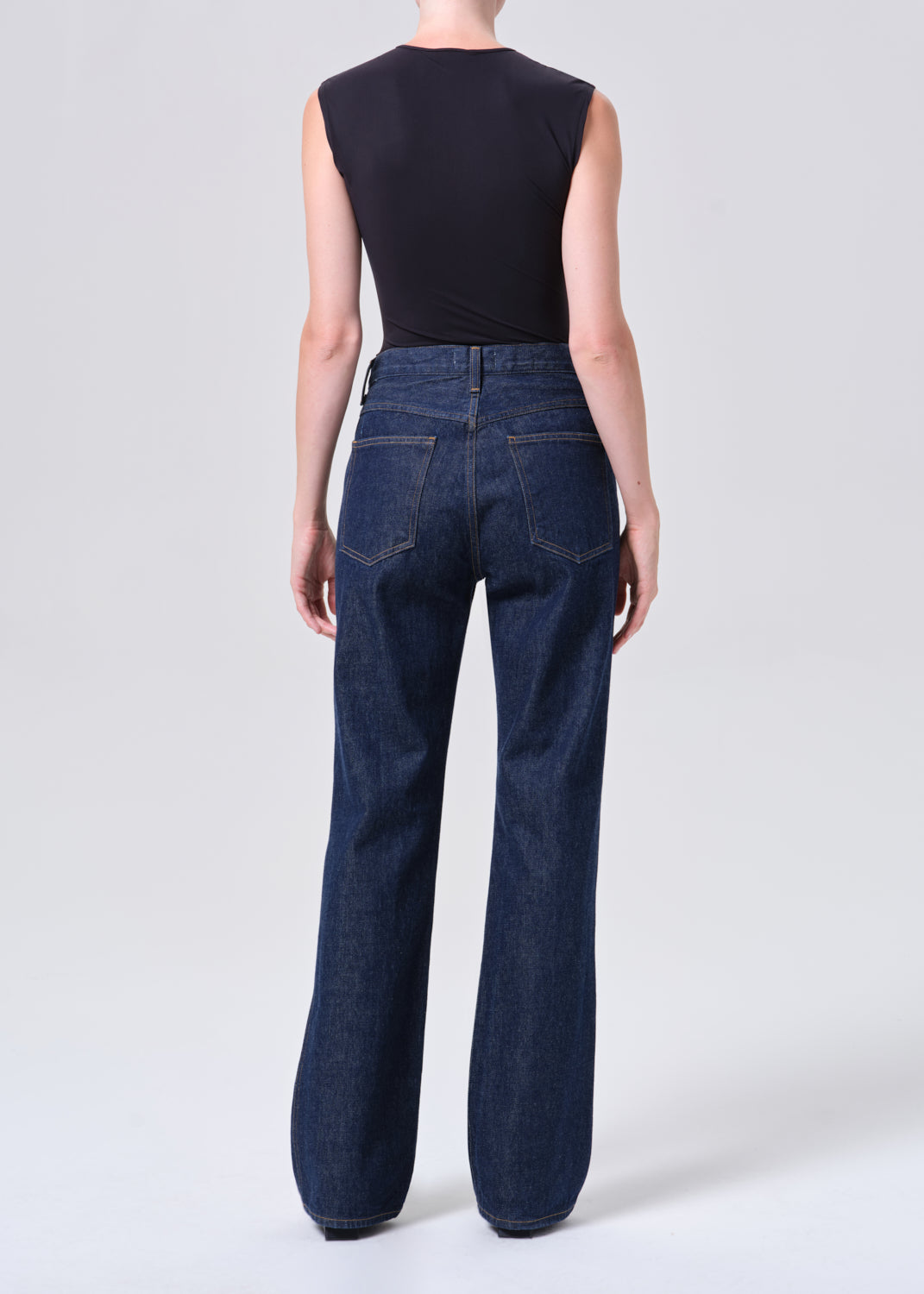 Person wearing dark blue jeans and a black sleeveless top on a white background