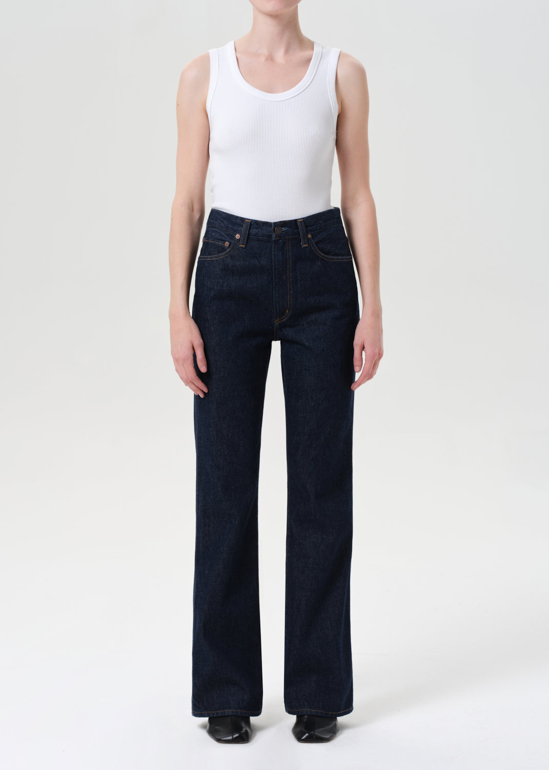 Person wearing a white tank top and dark blue jeans on a white background