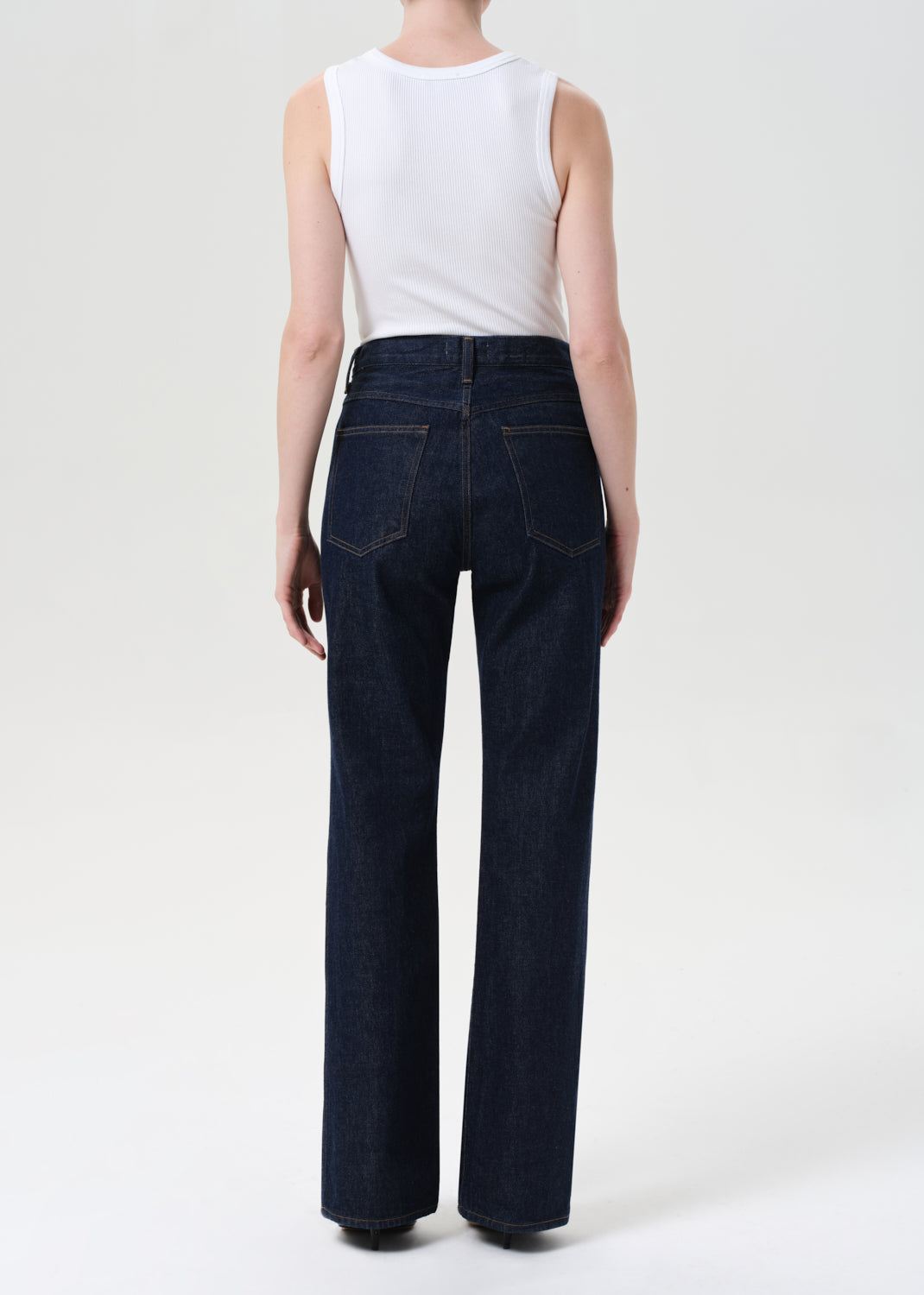 Person wearing dark blue jeans and a white top on a white background